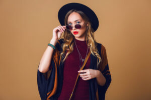 studio-close-up-portrait-young-fresh-blonde-woman-brown-straw-poncho-wool-black-trendy-hat-round-glasses-looking-camera-green-leather-had-bag